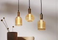 Trzy lampy wiszące z dekoracyjnymi żarówkami LED filament w ryflowanych bursztynowych kloszach nad stołem.
