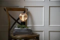 Lampa stołowa z dekoracyjną żarówką LED filament w kulistej ryflowanej bańce ustawiona na książkach na drewnianym krześle.