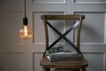 Wisząca lampa z dekoracyjną żarówką LED filament w kulistej ryflowanej bańce nad drewnianym krzesłem i książkami.