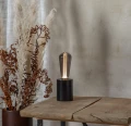 Lampa stołowa z dekoracyjną żarówką LED filament w przydymionej bańce ustawiona na drewnianym stole obok suszonych roślin.