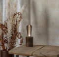 Lampa stołowa z dekoracyjną żarówką LED filament w przydymionej bańce ustawiona na drewnianym postumencie.