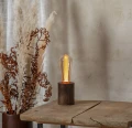 Lampa stołowa z dekoracyjną żarówką LED filament w bursztynowej bańce ustawiona na drewnianym postumencie na drewnianym stole.