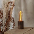 Lampa stołowa z dekoracyjną żarówką LED filament w bursztynowej bańce ustawiona na drewnianym stole obok suszonych roślin.