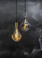 Dwie dekoracyjne żarówki LED z bursztynowego i przydymionego szkła zawieszone na przewodach przed ciemnym, teksturowanym tłem.