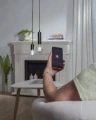 Sterowanie żarówką LED smart E27 za pomocą aplikacji mobilnej, widok ręki z telefonem i wiszących lamp w salonie.