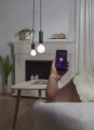 Sterowanie inteligentną żarówką LED E27 za pomocą aplikacji mobilnej, widok dłoni z telefonem i wiszących lamp w salonie.