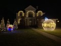 Elegancka iluminacja świąteczna domu – fasada ozdobiona ciepłymi światłami LED, w ogrodzie świecąca bombka 3D oraz dekoracyjny prezent i choinki, tworzące efektowną, przytulną aranżację na zewnątrz.