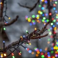 Kolorowe lampki LED owinięte wokół gałęzi drzewa, z rozmytym tłem wypełnionym światłami w barwach RGB.