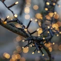 Zbliżenie na przewód świetlny LED owinięty wokół gałęzi, z licznymi punkcikami ciepłego światła i efektem bokeh w tle.
