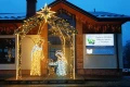 Szopka świetlna 3D z postaciami Świętej Rodziny, ustawiona przed Gminnym Ośrodkiem Kultury i Biblioteką w Polańczyku, oświetlona dekoracjami świątecznymi na tle budynku z zimowym krajobrazem.