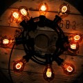 Girlanda ogrodowa z żarówkami LED TA60 2,5W 2000K z serii Decoled Amber, świecącymi ciepłym, dekoracyjnym światłem na tle drewnianej szpuli, przewód czarny z czarnymi oprawkami.
