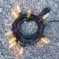 Girlanda ogrodowa z żarówkami LED T45 2,8W 2200K z serii Decoled Amber, ułożona na szarym żwirze. Żarówki emitują ciepłe, dekoracyjne światło i osadzone są w czarnych oprawkach na elastycznym kablu.
