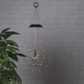 Wisząca dekoracja solarna FIREWORK® z ciepłobiałymi diodami LED na tle jasnej ceglanej ściany. Promienista forma przypomina rozświetlony fajerwerk.