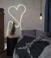 Wąż LED biały uformowany w kształt serca na ścianie nad łóżkiem w sypialni, tworzący przytulną atmosferę.