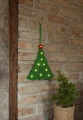 Zielona filcowa choinka LED z podświetlanymi gwiazdkami i czerwoną gwiazdą na górze zawieszona na ceglanej ścianie obok doniczki z zieloną rośliną.