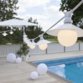 Biała girlanda CONNECTA z kulistymi żarówkami E27 rozwieszona nad tarasem przy basenie. Oświetlenie tworzy jasną, elegancką atmosferę w przestrzeni zewnętrznej.