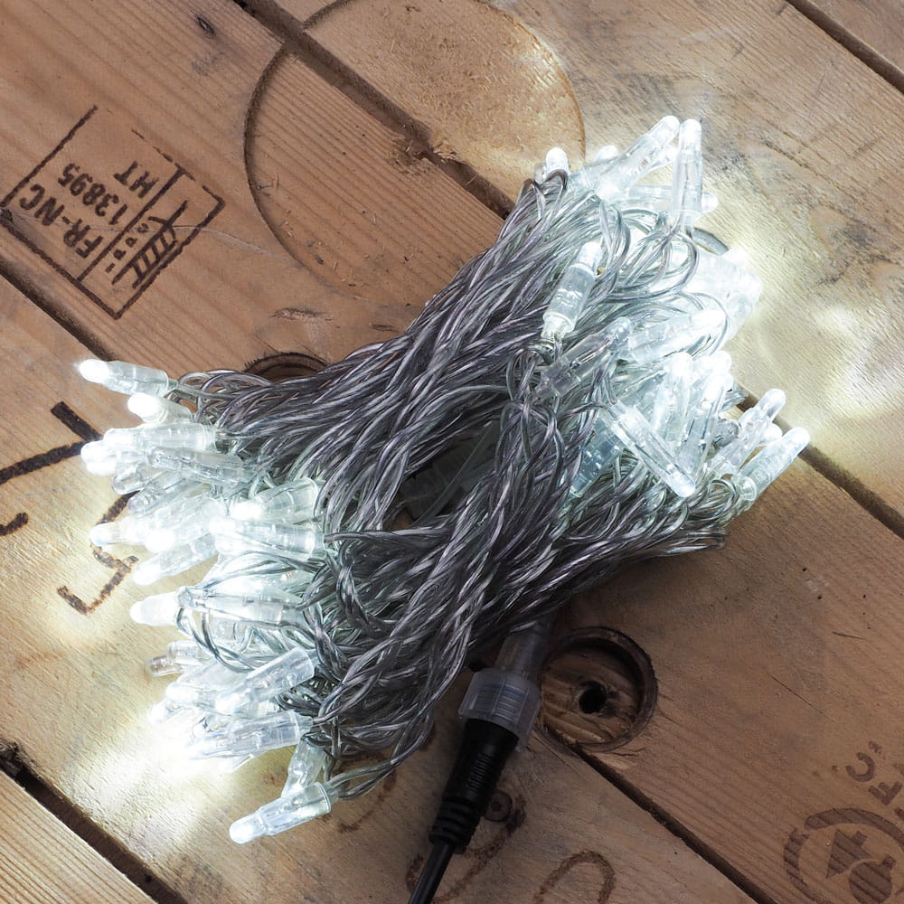 Zwinięty przewód świetlny z dziesiątkami zimnobiałych lampek LED, leżący na drewnianej skrzyni z widocznymi oznaczeniami transportowymi.