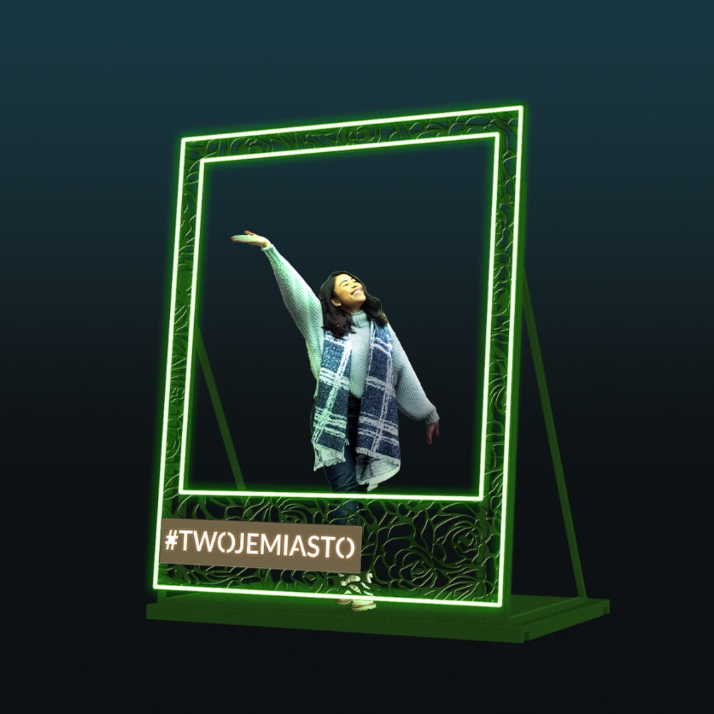 Dekoracyjna ramka LED w stylu polaroid na ciemnym tle z podświetlaną zieloną konstrukcją i miejscem na napis, nowoczesny fotopunkt do eventów, galerii handlowych i przestrzeni miejskich przyciągający uwagę.