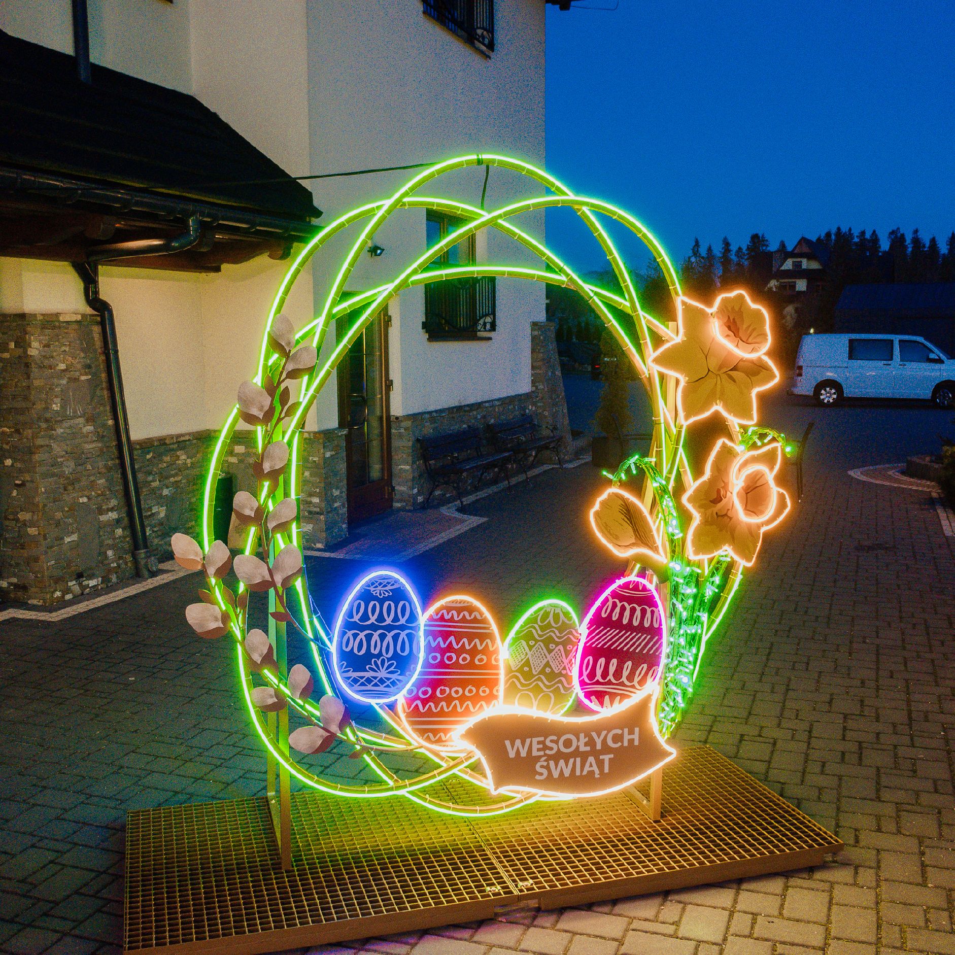 Bramka Wiosna 3D LED ustawiona przed budynkiem, świetlna dekoracja wielkanocna z pisankami i żonkilami, napis Wesołych Świąt, instalacja zewnętrzna na metalowej podstawie.