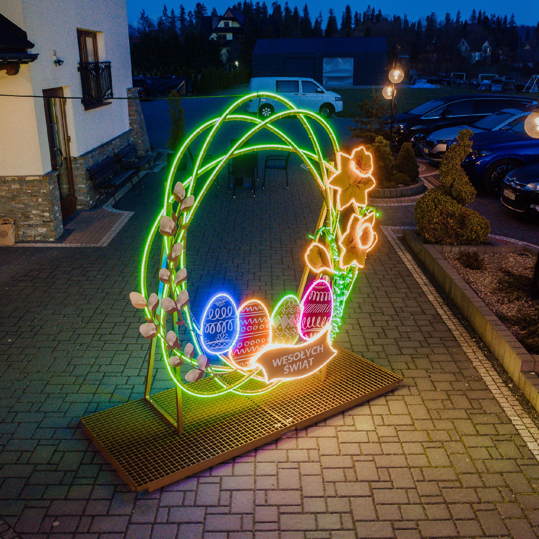 Bramka Wiosna 3D LED ustawiona przed budynkiem, świetlna dekoracja wielkanocna z pisankami i żonkilami, napis Wesołych Świąt, instalacja zewnętrzna na metalowej podstawie.