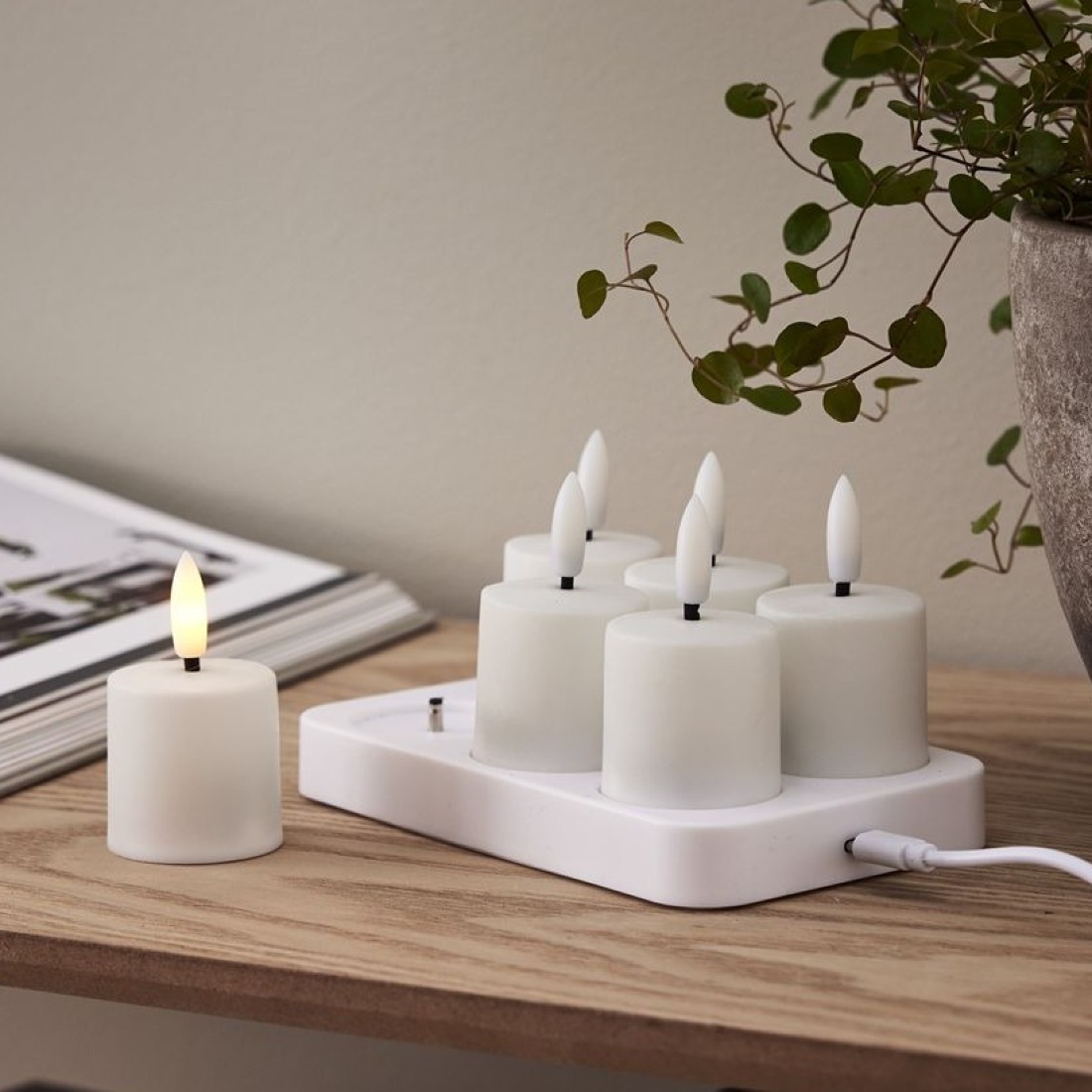 Świeczki LED tealight na bazie ładującej, jedna świeczka zapalona obok.