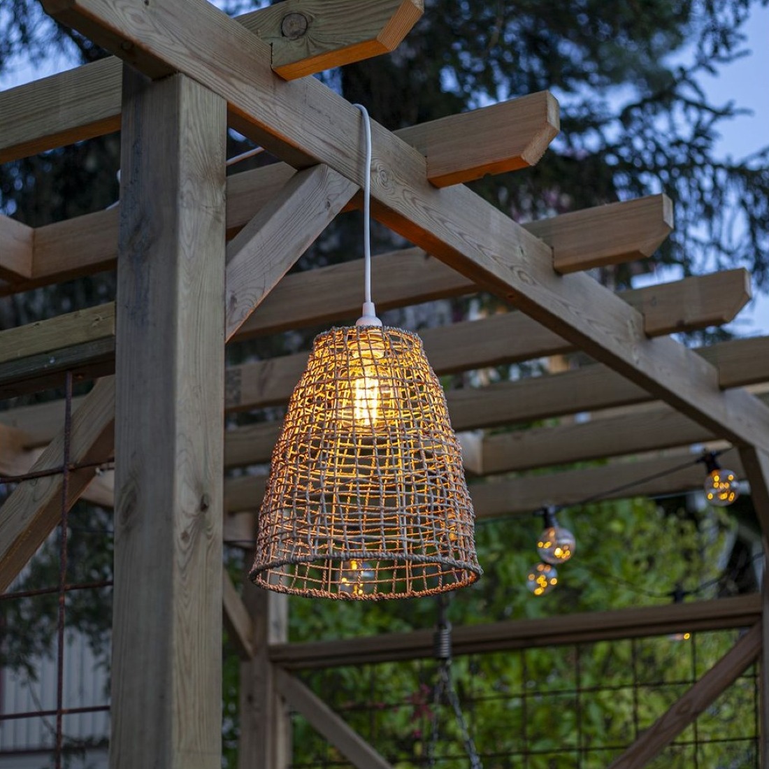 Lampa wisząca z rattanowym kloszem w altanie ogrodowej, ciepłe światło LED tworzy przytulny nastrój.