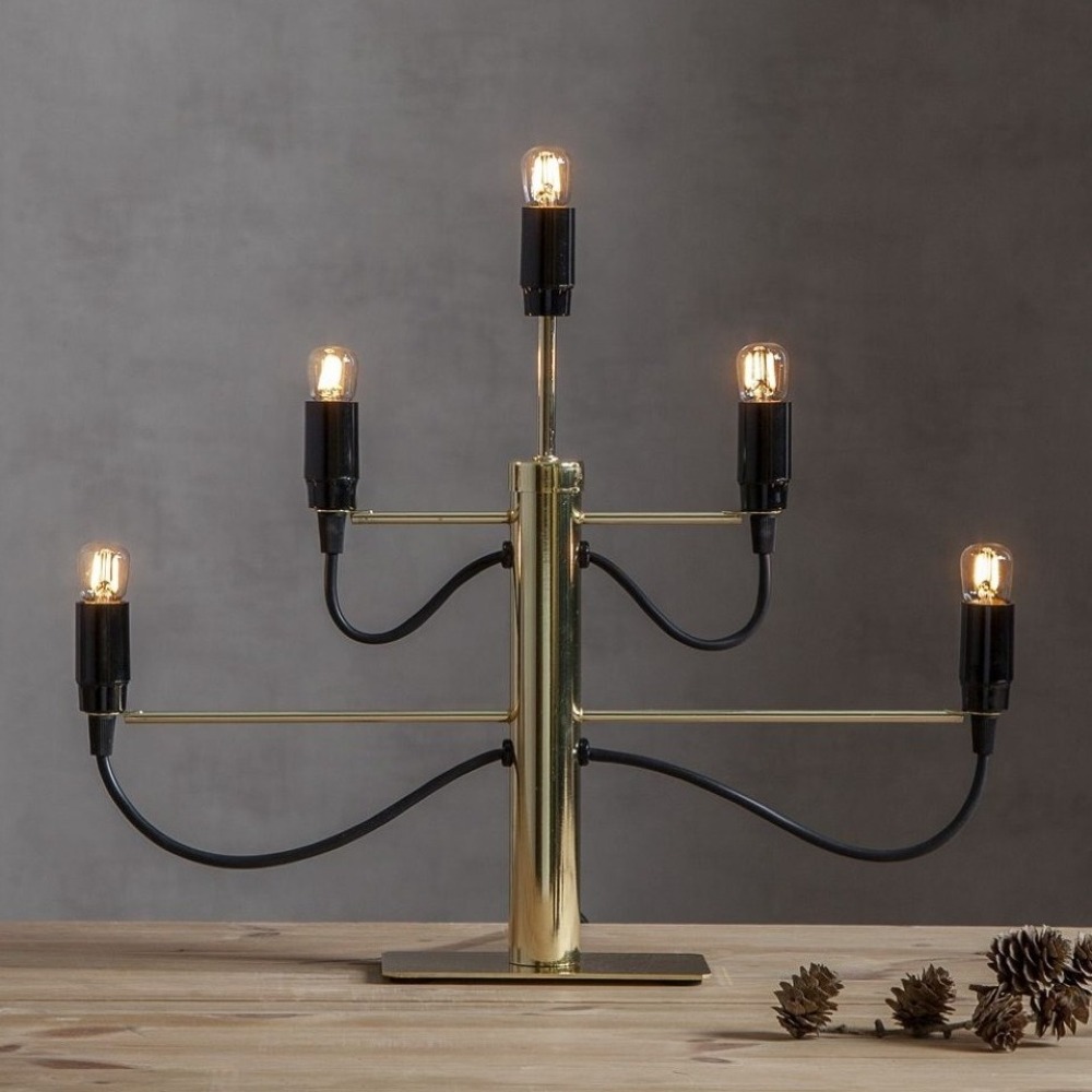 Złoty świecznik elektryczny z pięcioma żarówkami LED, ustawiony na stole obok szyszek, aranżacja wnętrzarska.