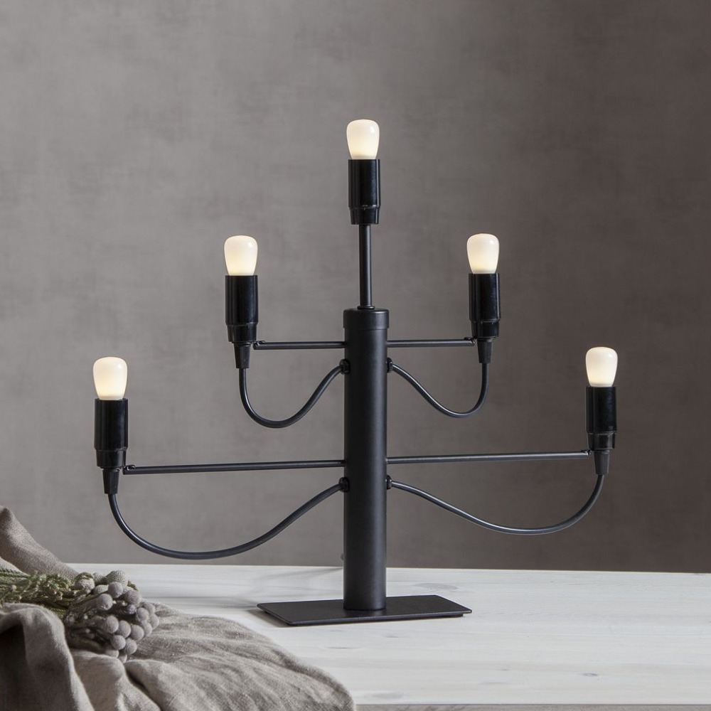 Czarny świecznik elektryczny z pięcioma żarówkami LED, ustawiony na stole obok szyszek, aranżacja wnętrzarska.