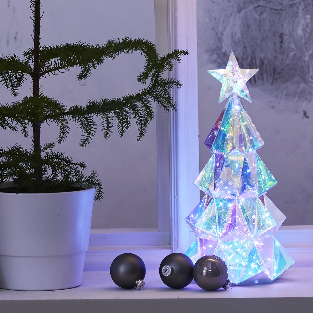 Podświetlana choinka LED o geometrycznej formie stoi na parapecie przy oknie, obok doniczki z zieloną rośliną oraz trzech matowych, czarnych bombek, tworząc spokojną, zimową aranżację wnętrza.