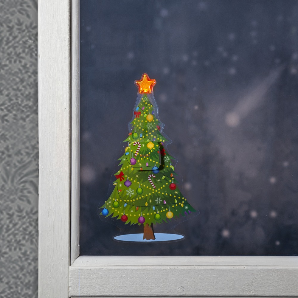 Naklejka LED przedstawiająca ozdobioną choinkę ze świecącą gwiazdą, przyklejona do szyby w białej ramie, z zimowym, rozmytym tłem za oknem.