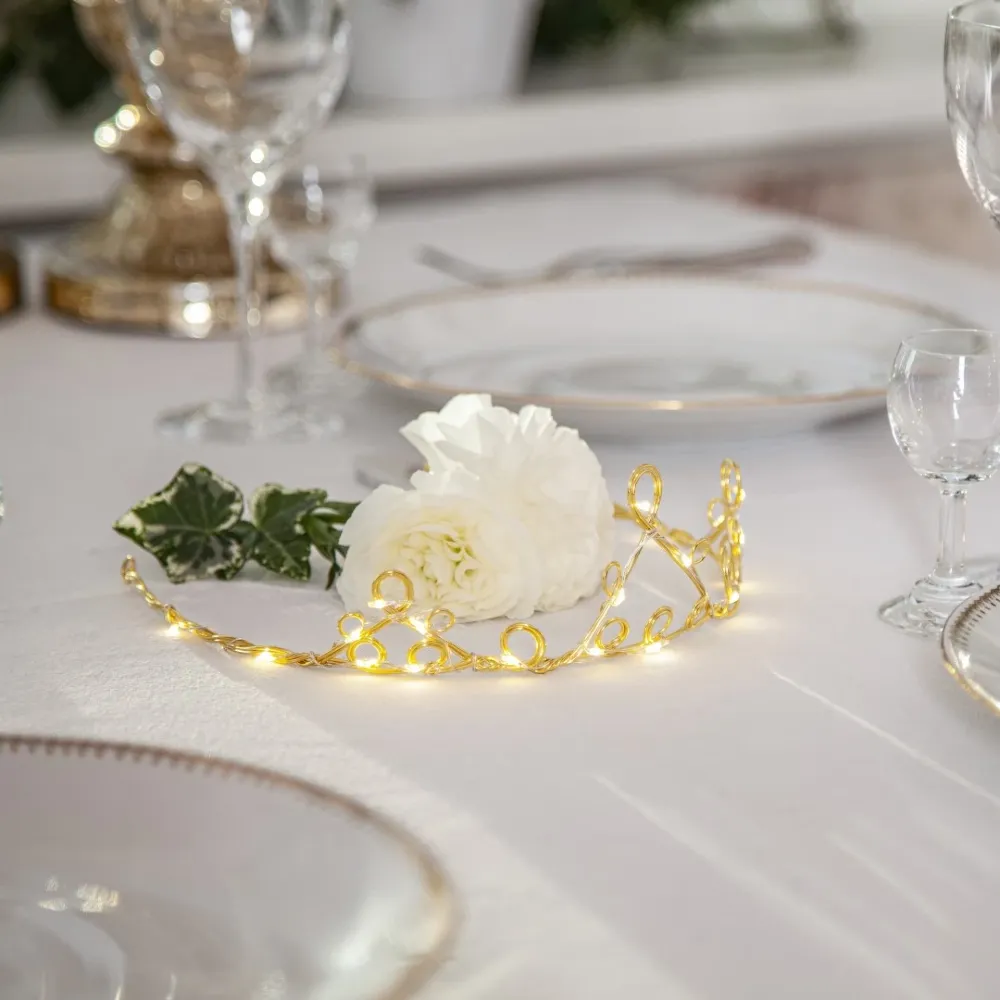 Mosiężny diadem LED wkomponowany w jasną, świąteczną aranżację z kwiatem i szkłem, wprowadzający subtelny, nastrojowy klimat.