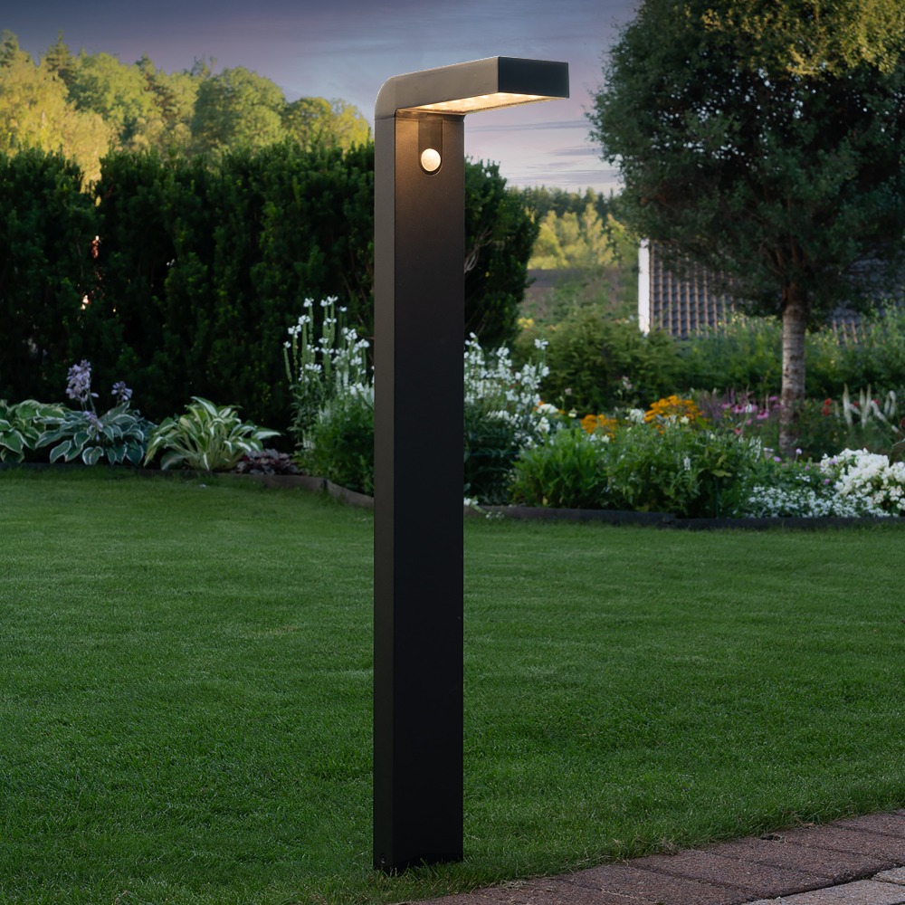Czarna solarna lampa ogrodowa LED VICI w formie słupka z czujnikiem ruchu PIR zamontowana na trawniku nowoczesne oświetlenie zewnętrzne do ogrodu.