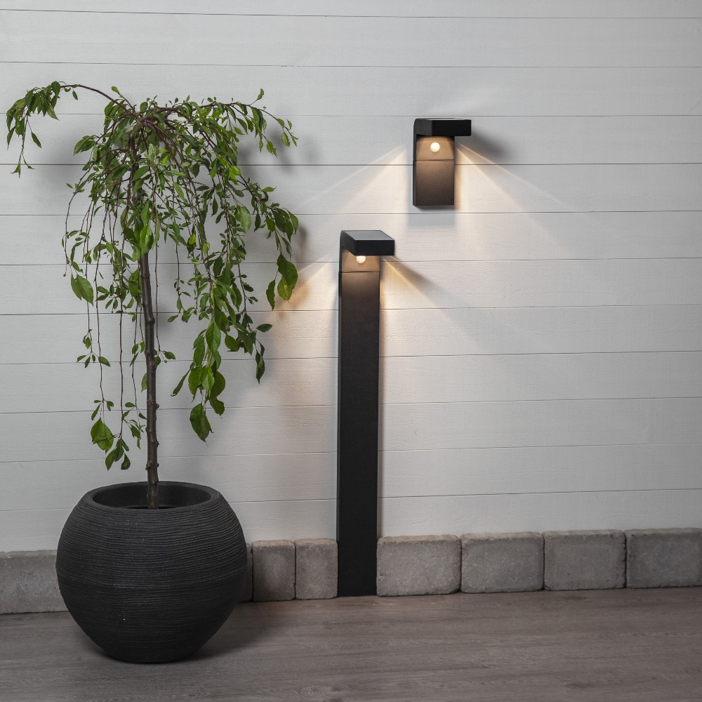 Czarna solarna lampa ogrodowa LED VICI w formie słupka oraz kinkiet ścienny tworzące spójne oświetlenie nowoczesnej przestrzeni przy domu.