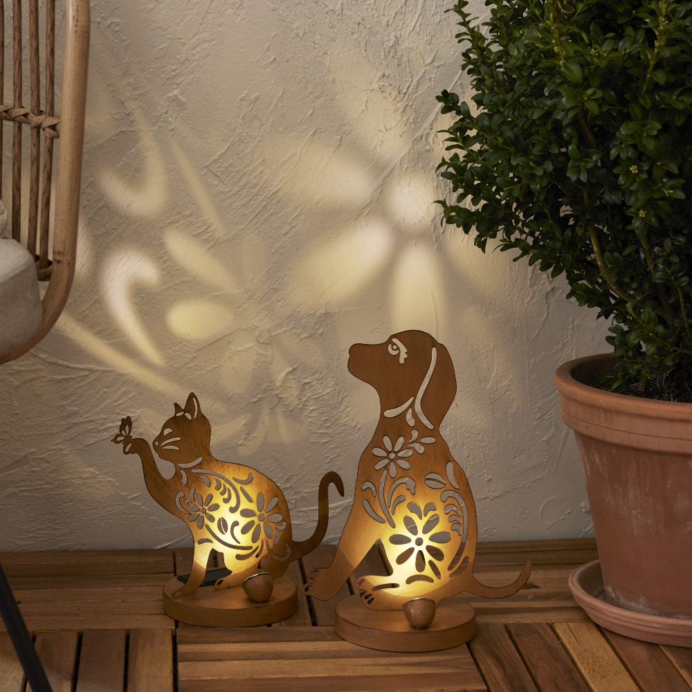 Solarne lampy ogrodowe LED w kształcie kota i psa z dekoracyjnym wycinanym wzorem, ustawione na drewnianym tarasie. Ozdoby solarne z podświetleniem tworzące efekt świetlnych wzorów na ścianie, dekoracja do ogrodu, na taras lub balkon.