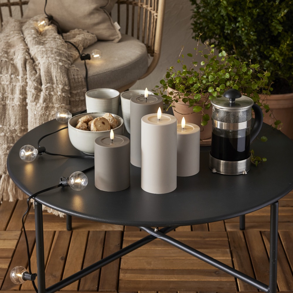 Solarna girlanda świetlna LED z dekoracyjnymi żarówkami w ciepłej barwie ułożona na czarnym stoliku tarasowym obok świec, filiżanek i zaparzacza do kawy. Oświetlenie solarne do ogrodu, na balkon lub taras.