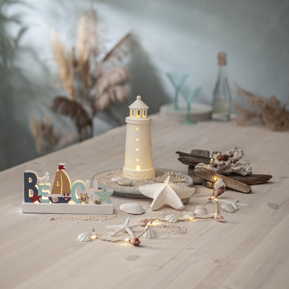 Drewniana dekoracja Beach LED w aranżacji z porcelanową latarnią i rozgwiazdą wśród muszli i dekoracji w stylu seaside.