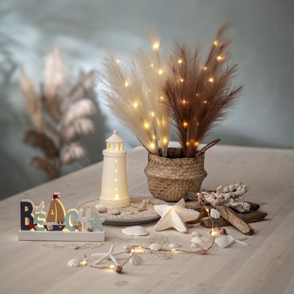 Dekoracja w stylu nadmorskim z porcelanową rozgwiazdą LED na stole wśród muszli drewna i latarni emitująca ciepłe światło.