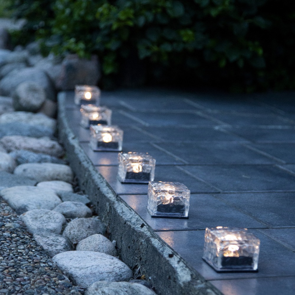 Rząd solarnych lamp LED w kształcie kostek ustawionych wzdłuż ścieżki ogrodowej.