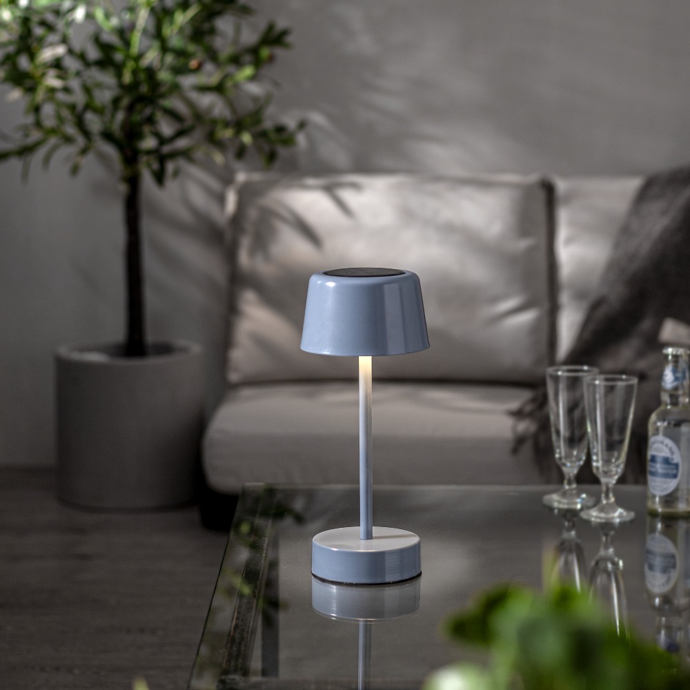 Niebieska lampa stołowa LED solarna z możliwością ładowania przez USB, ustawiona na stoliku w eleganckim wnętrzu.