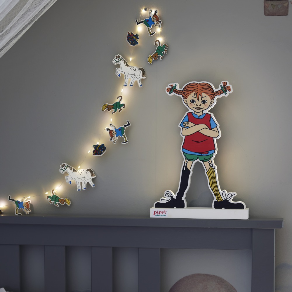 Girlanda świetlna Pippi zawieszona nad łóżkiem obok sylwetki bohaterki, tworzy spójną, bajkową aranżację i przytulnie rozświetla przestrzeń.