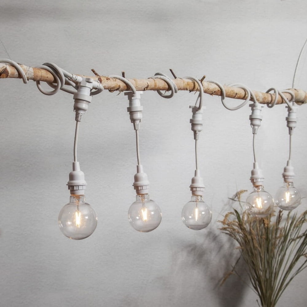 Detal girlandy CONNECTA z białym kablem i oprawkami E27 zawieszonymi na drewnianej belce, z widocznym prowadzeniem przewodu.