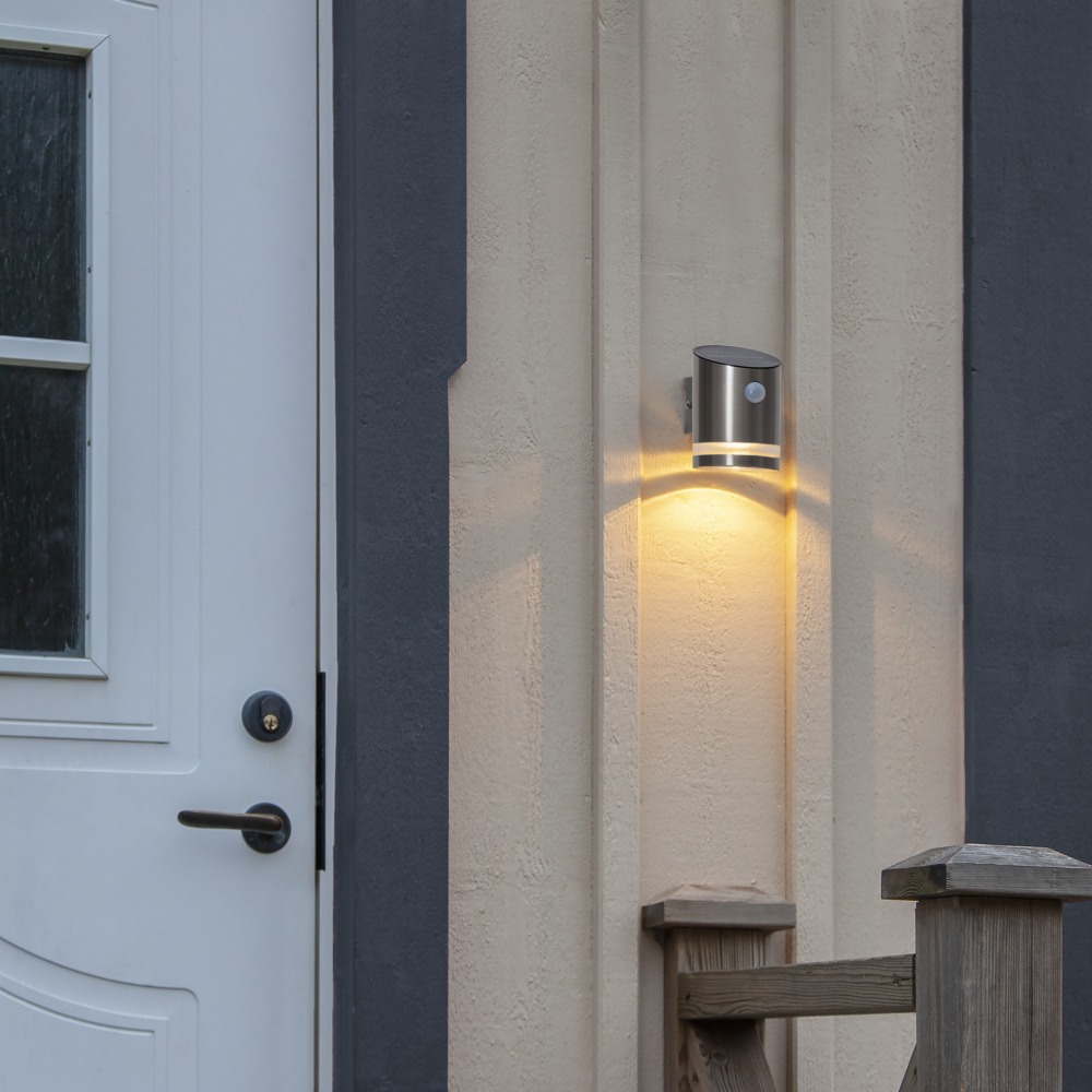 Kinkiet solarny przy drzwiach z czujnikiem ruchu, zapewnia funkcjonalne oświetlenie i przyjemny, rozproszony efekt świetlny.