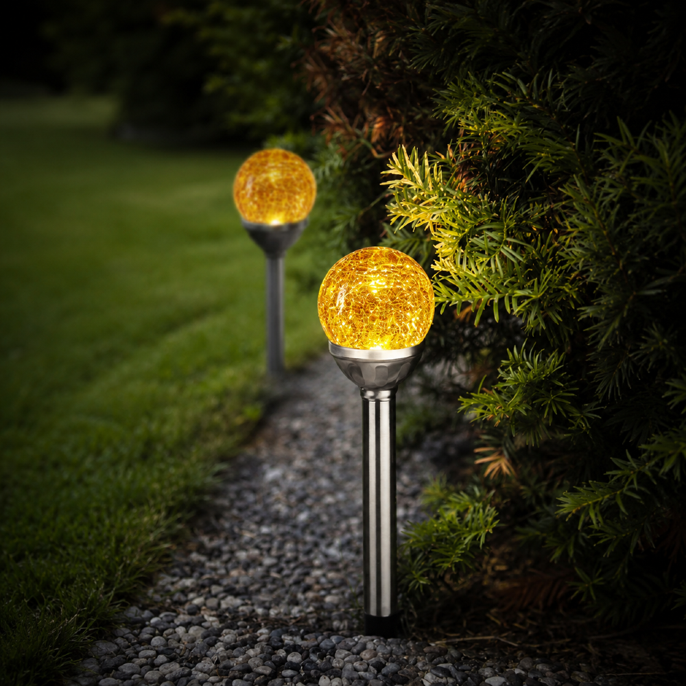 Dwie solarne lampy ogrodowe LED z bursztynowymi kulami o efekcie spękanego szkła oświetlające ścieżkę w ogrodzie, dekoracyjne oświetlenie zewnętrzne z ciepłym światłem.