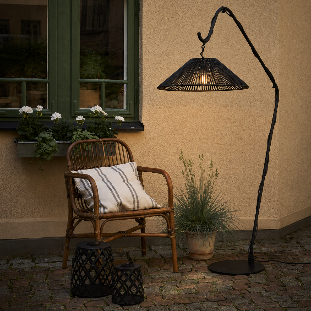Lampiony solarne w czarnym kolorze obok fotela i stojącej lampy ogrodowej na klimatycznym patio po zmroku.