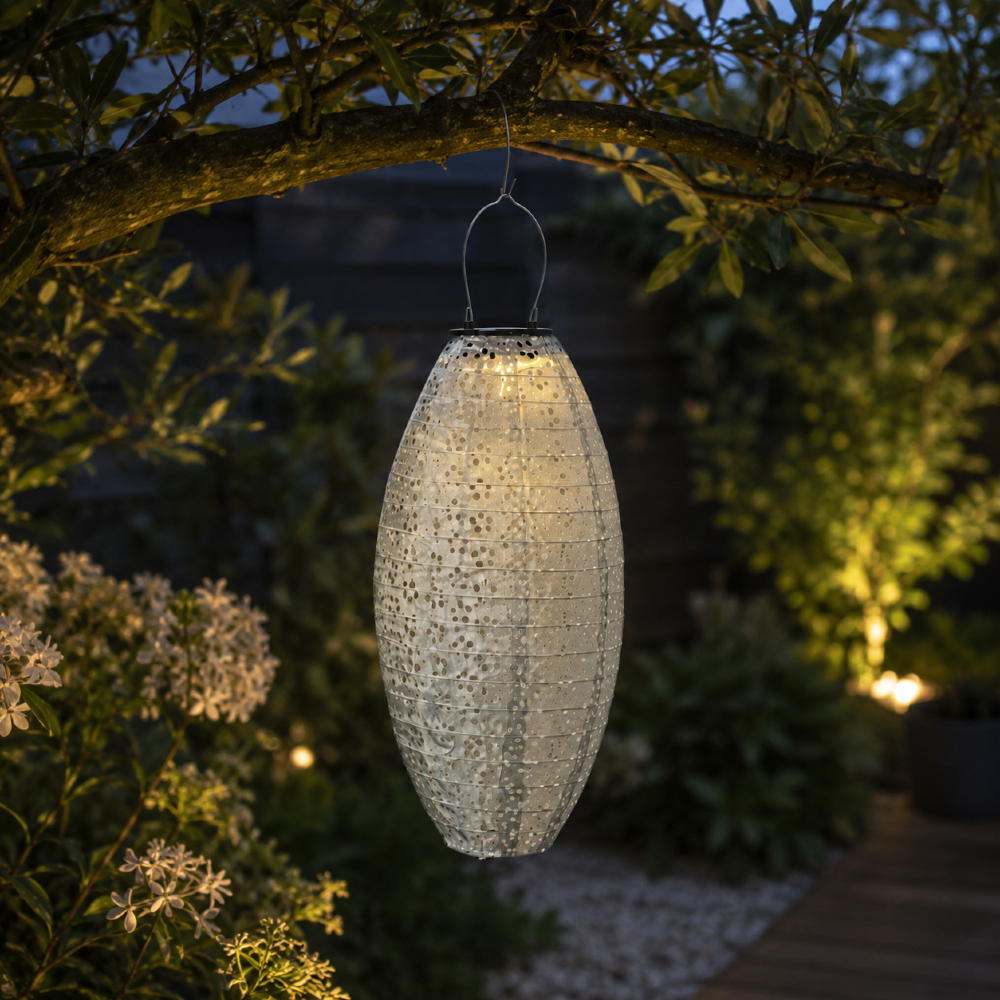 Podłużny lampion solarny LED zawieszony na gałęzi drzewa w ogrodzie. Ciepłe światło podkreśla rośliny i tworzy dekoracyjne refleksy po zmroku.