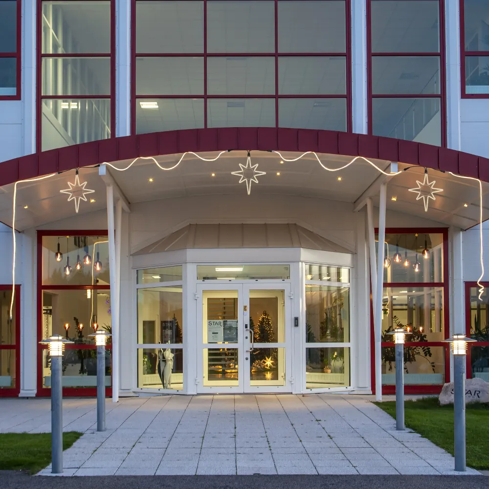 Trzy podświetlane gwiazdy rozmieszczone nad wejściem do budynku, uzupełnione dekoracyjnym oświetleniem biegnącym pod zadaszeniem.