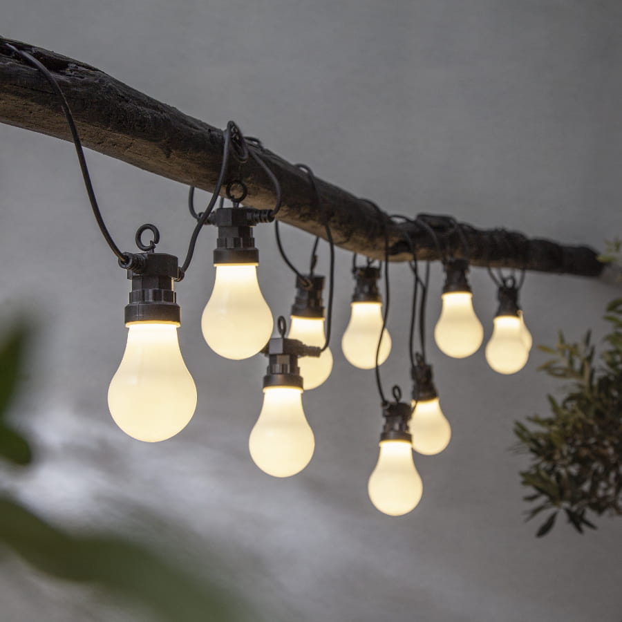 Girlanda ogrodowa LED z mlecznymi kloszami zawieszona na drewnianej belce, emitująca ciepłe, nastrojowe światło, idealna do oświetlenia tarasu lub altany.