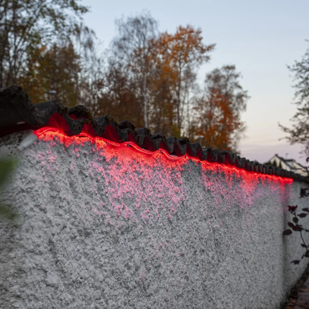 Czerwony wąż LED zamocowany wzdłuż krawędzi dachu budynku, emitujący intensywne światło w półmroku.