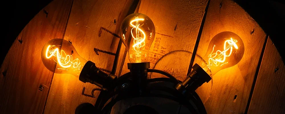 Girlanda świetlna z żarówkami LED A60 w dymionym szkle emitującymi bardzo ciepłe światło 1800K, spiralne żarniki, klimatyczna aranżacja vintage na drewnianym tle.